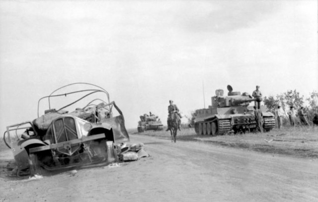 Two Panzer Mk VI Tiger tanks, a destroyed vehicle and a German on a horse – By Bundesarchiv – CC BY-SA 3.0