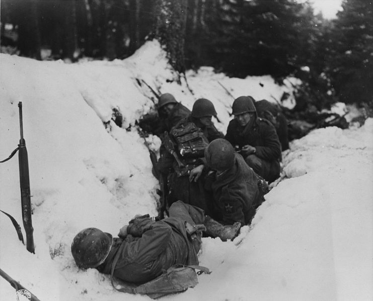 U.S. infantrymen crouch in a snow-filled ditch, taking shelter from a German artillery barrage during the Battle of Heartbreak Crossroads in the Krinkelter woods on 14 December 1944.