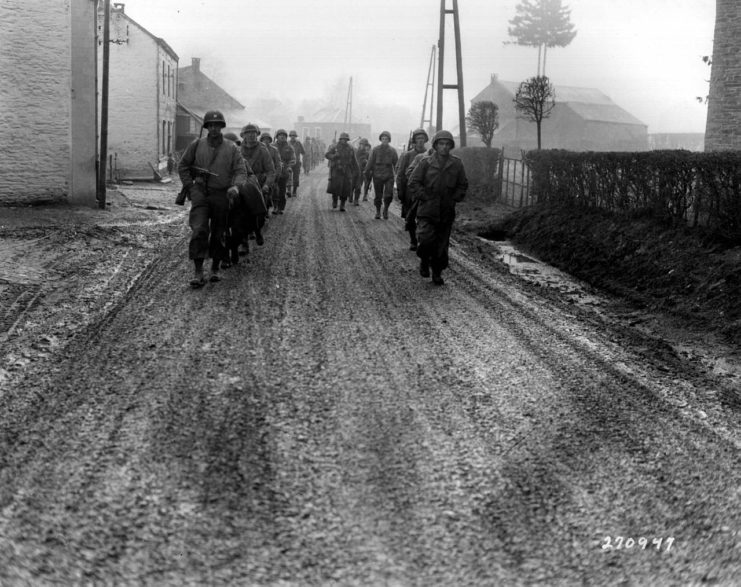 U.S. troops of the 28th Infantry Division, who have been regrouped in security platoons for the defense of Bastogne, Belgium, march down a street in Bastogne.