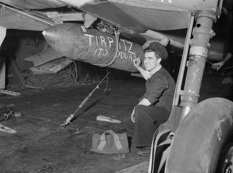 A sailor aboard HMS FURIOUS chalks a message on a bomb slung beneath an aircraft due to take part in the attack on the TIRPITZ in Alten Fjord, Norway, 3 April 1944.
