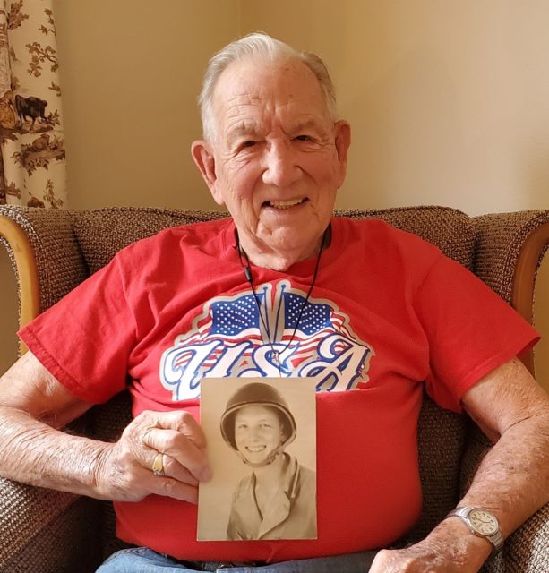 Herb Meyer in the present day, smiling while holding a photo from his army years