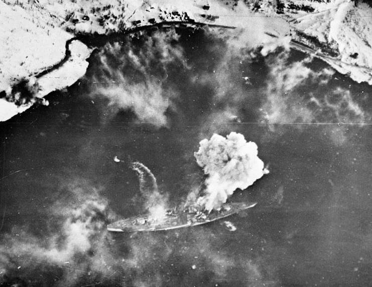 The wake of a fast moving motor boat as she hurries away from the battered Tirpitz can be seen as a huge cloud rises from an early bomb hit on the German battleship.