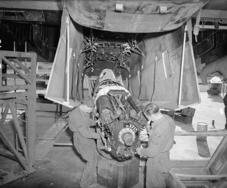 Two RAF fitters at work on the Rolls Royce Merlin engine of a Supermarine Spitfire, beneath the bomb bay of a Handley Page Halifax converted for the purpose of carrying a Spitfire fuselage.