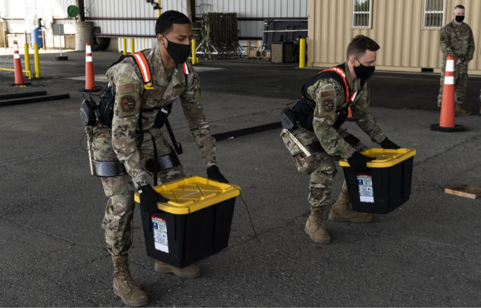 Airman 1st Class Xaviar Archangel and Airman 1st Class Kyle Sunderman lifting boxes while wearing Aerial Porter Exoskeletons