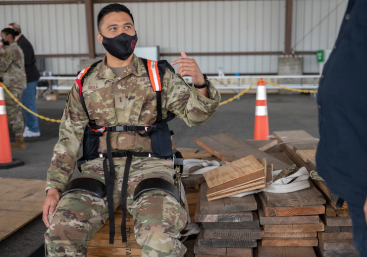 2nd Lt. Germaine Seisa sitting on a pile of wood while wearing an Aerial Porter Exoskeleton