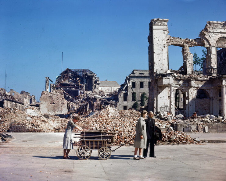 Family walking with a wagon past destroyed buildings and rubble