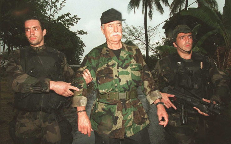 Bob Denard being taken into custody by two French soldiers