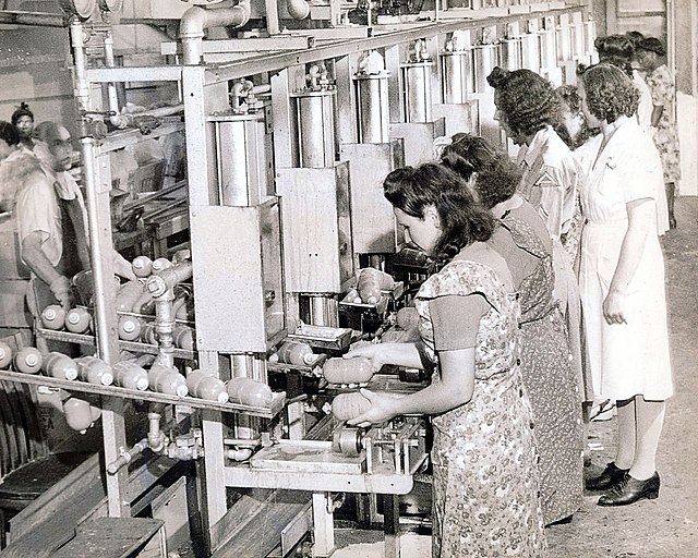 Women filling bug bombs as they roll down an assembly line