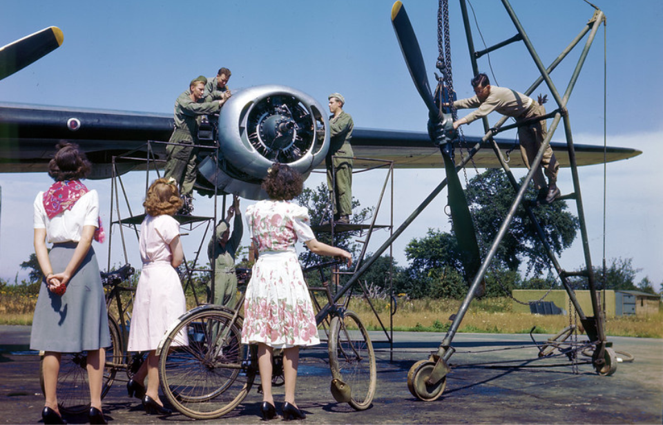 Three women watching men with the Eighth Air Force perform maintenance on a Consolidated B-24 Liberator