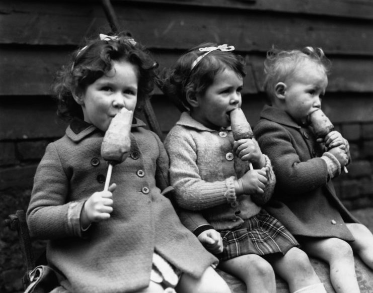 three young children eating carrots on a stick 