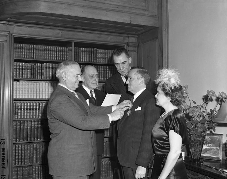 Bill Donovan pinning the Medal of Merit to William Stephenson's chest, while a woman and two men stand around them