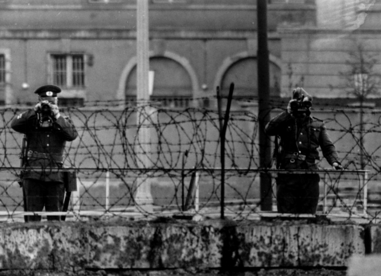 Zwei ostdeutsche Polizisten blicken über den Stacheldraht auf der Berliner Mauer