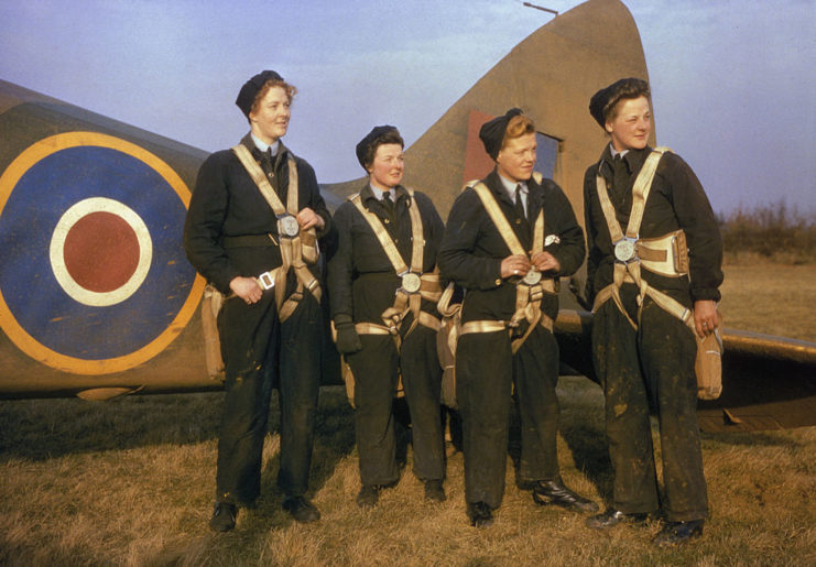 Female pilots wearing parachute gear in front of a British warplane