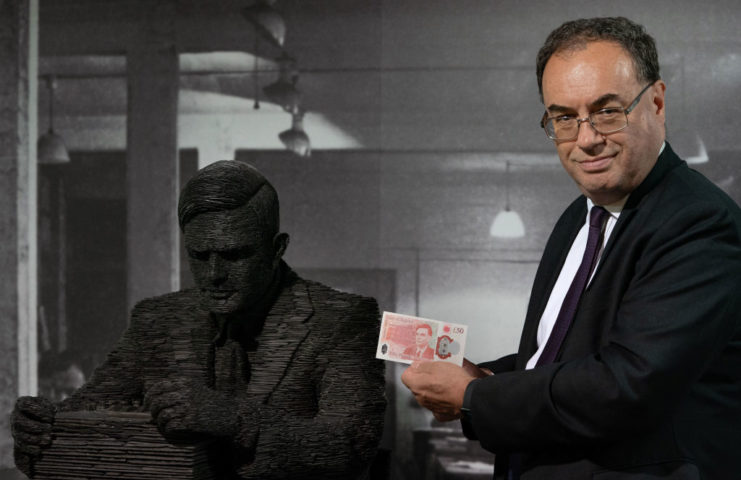 Governor Andrew Bailey holding the new banknote next to a statue of Alan Turing