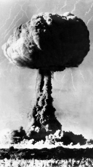 A black and white photograph of a mushroom cloud rising over the testing site at Maralinga in 1956