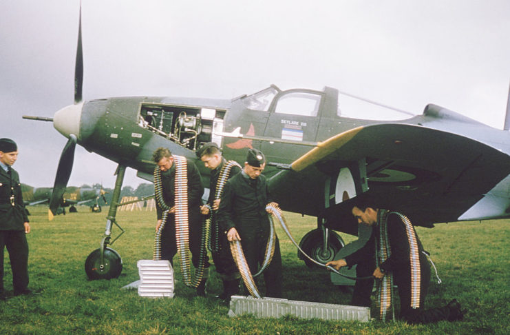 Royal Air Force (RAF) armorers standing next to a Bell P-39 Airacobra with ammunition belts around their shoulders