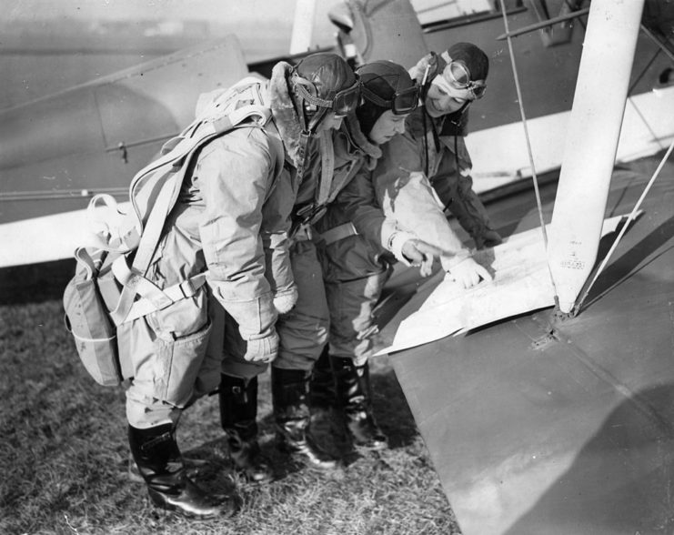 Margaret Cunnison, Rosemary Rees and Gabrielle Patterson reading a map laid out on the wing of an aircraft