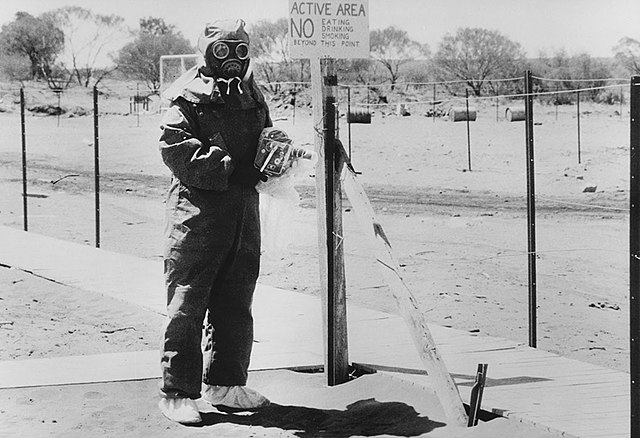 A black and white photograph of John L. Stanier in protective gear, holding a camera