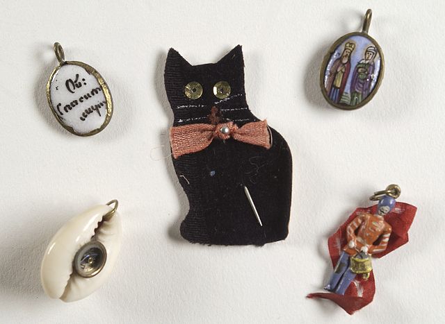 Selection of charms depicting a shell, a black cat, an individual, two holy people and text on a white pearl