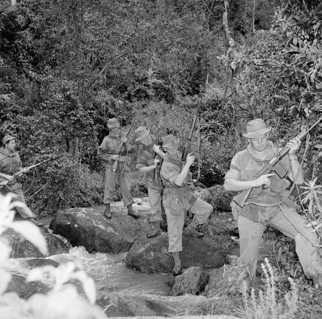 Five British soldiers navigating a rocky brush area