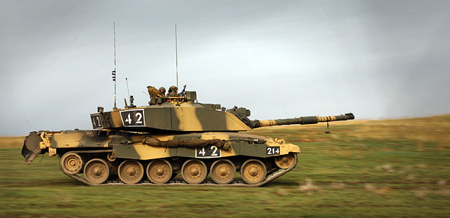 Camouflage-colored Challenger 2 tank driving on the grass under overcast skies