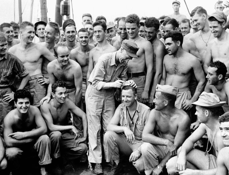 Ernie Pyle writing on a Marine's head, surrounded by a group of other Marines