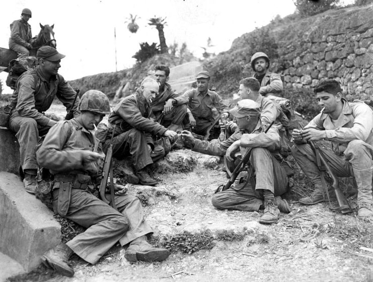 Ernie Pyle and numerous Marines sitting on the ground and smoking