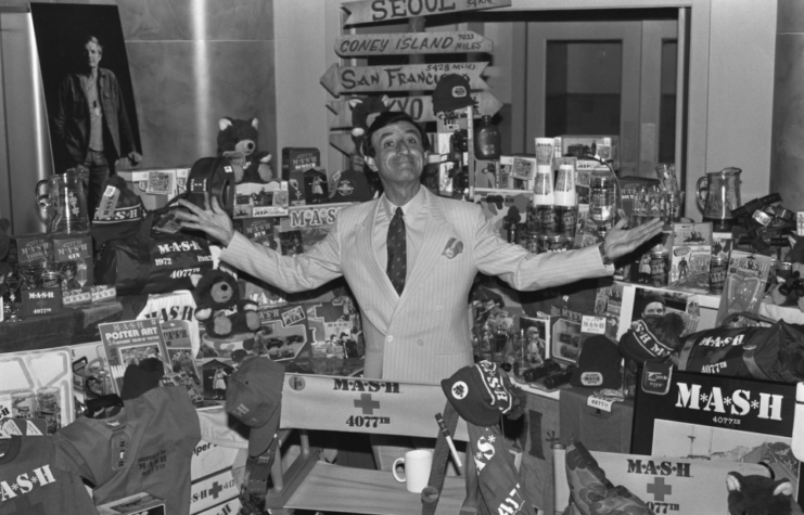 Actor Jamie Farr, who played Klinger in the T.V. show MASH, poses with some of the products spun off from the popular movie and T.V. show. Five hundred products, including everything from hats to teddy bears, carry the MASH logo.