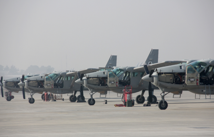 A fleet of Cessna 208 planes is parked on an airbase.