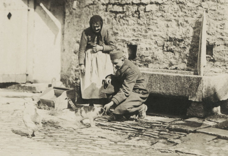 American soldier pets a cat while a French woman watches