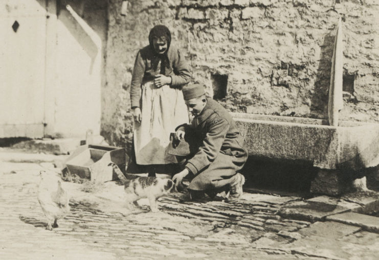 American soldier petting a cat while a French woman watches