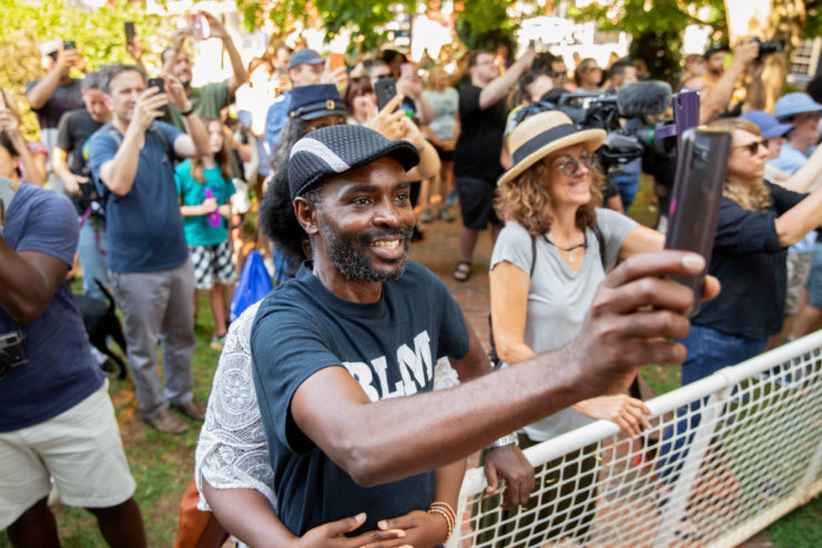 Citizen holding their phone up while surrounded by others watching the removal