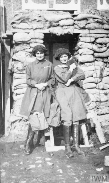 Two women standing outside a building with a cat in their arms