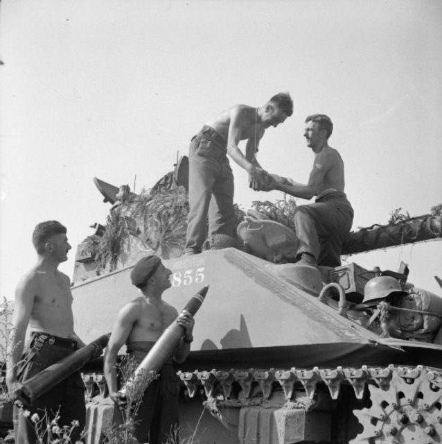 A Sherman Firefly crew of 1st Northamptonshire Yeomanry load ammunition for the 17-pounder gun into their vehicle before the start of Operation 'Totalise'.
