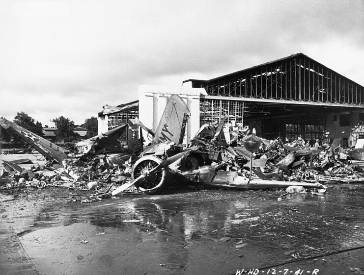 Destroyed aircraft and debris in front of an airport hangar