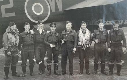 Sidney Baker standing in front of an airplane with seven airmen