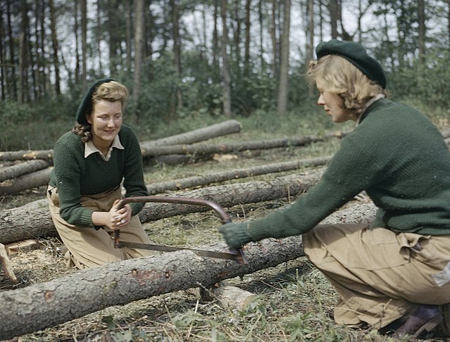 Two women in uniform using a handsaw to cut through a log