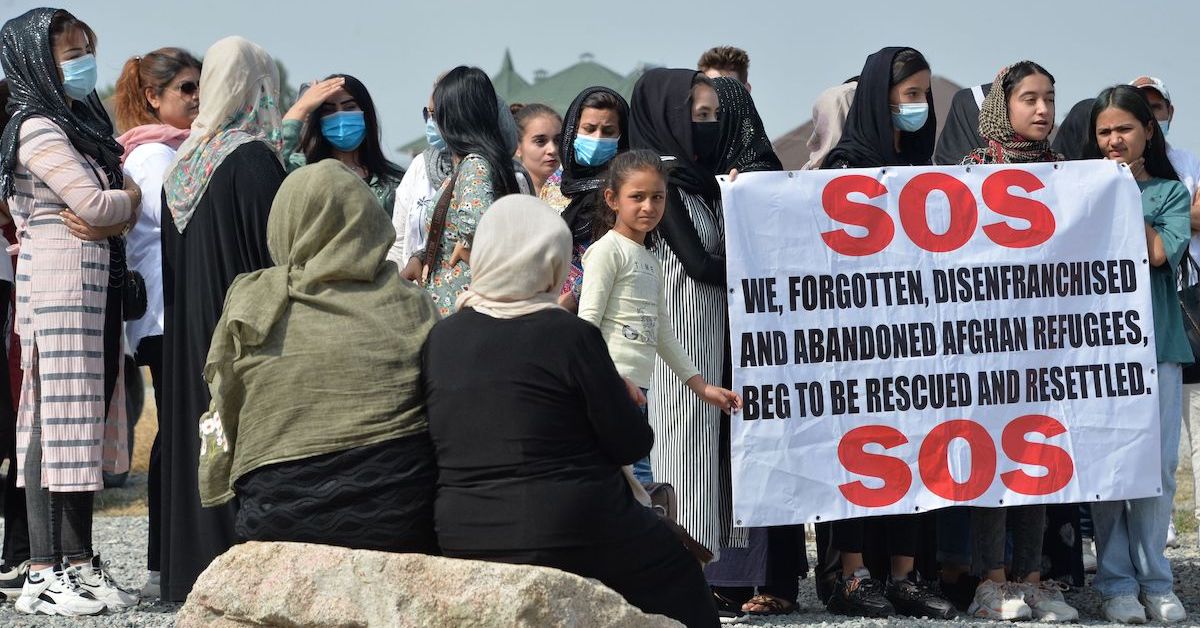 Women standing together, with one holding a sign requesting aid