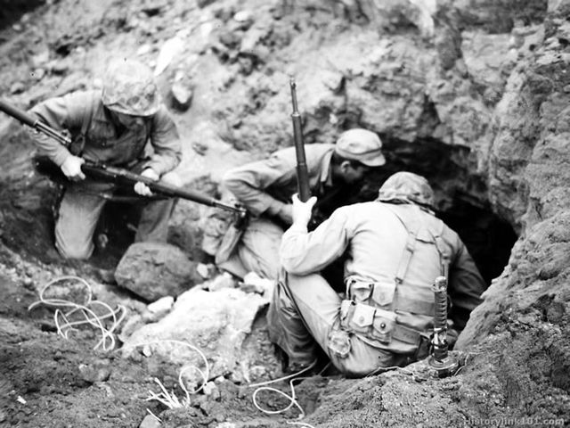 U.S. Marines crouched in front of a cave in the sand