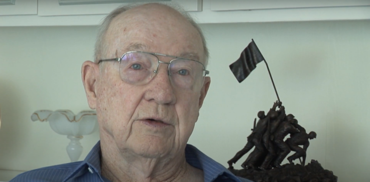 Colonel Dave Severance sitting beside a statue of the flag mounting