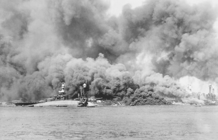 The capsized USS Oklahoma (BB-37) is visible the foreground of battleship row at Pearl Harbor