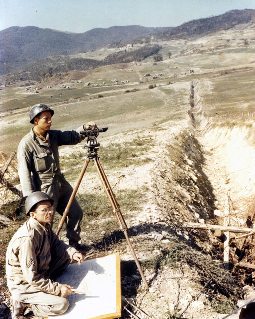 Two Army engineers standing beside surveying equipment
