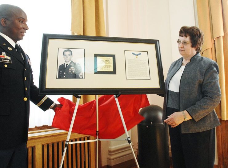 Betty Gordon and Lt. Colonel Eric Warner standing beside a plaque with Gary Gordon's image on it.
