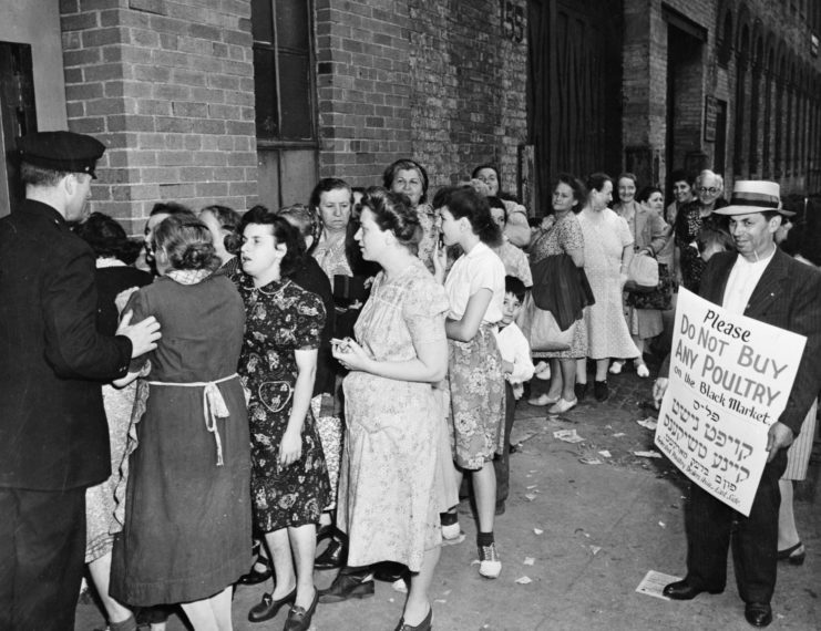 Women lined up outside of a building, with a man standing nearby, holding a protest sign
