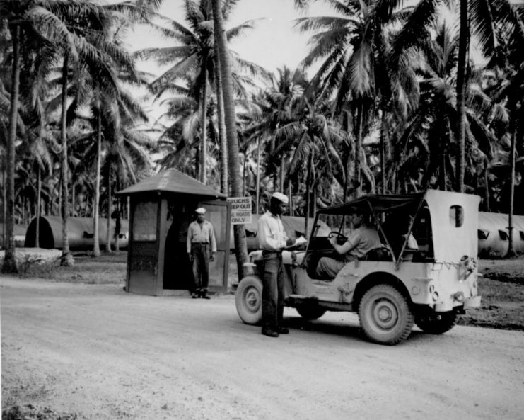 Enlisted man standing behind a military Jeep, while another man stands at the entrance to a roadside booth