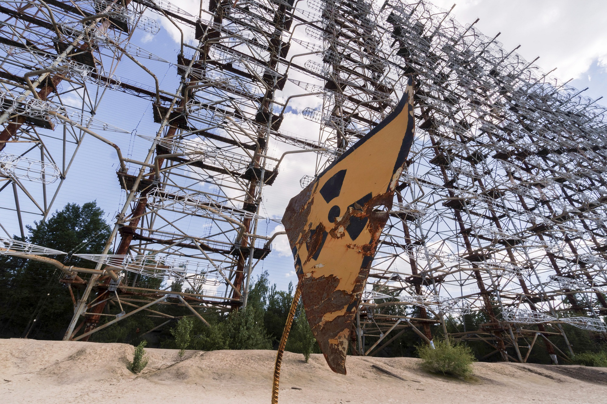 A rusty radioactivity warning sign sits beneath the inter-ballistic early warning radar system, known as Duga Radar, in the Chernobyl exclusion zone in Chernobyl, Ukraine, on Wednesday, June 19, 2019. (Photo Credit: Vincent Mundy/Bloomberg via Getty Images)