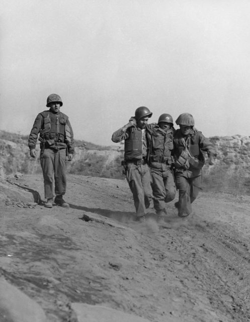 Two soldiers supporting an injured soldier, while another walks beside them