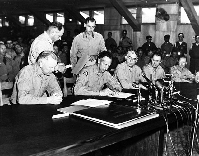 General Clark signing the Korean Armistice Agreement while military officials watch
