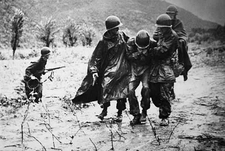 Emil Kapaun and another soldier carrying an exhausted troop through the mud