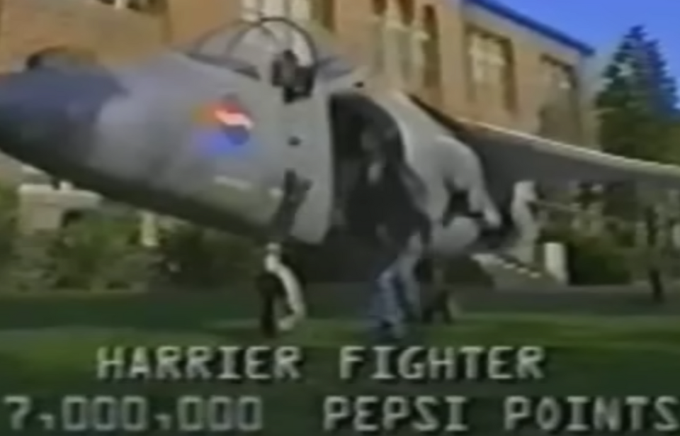 Teenager jumping out of the cockpit of a McDonnell Douglas AV-8B Harrier II, with "HARRIER FIGHTER 7,000,000 PEPSI POINTS" written below